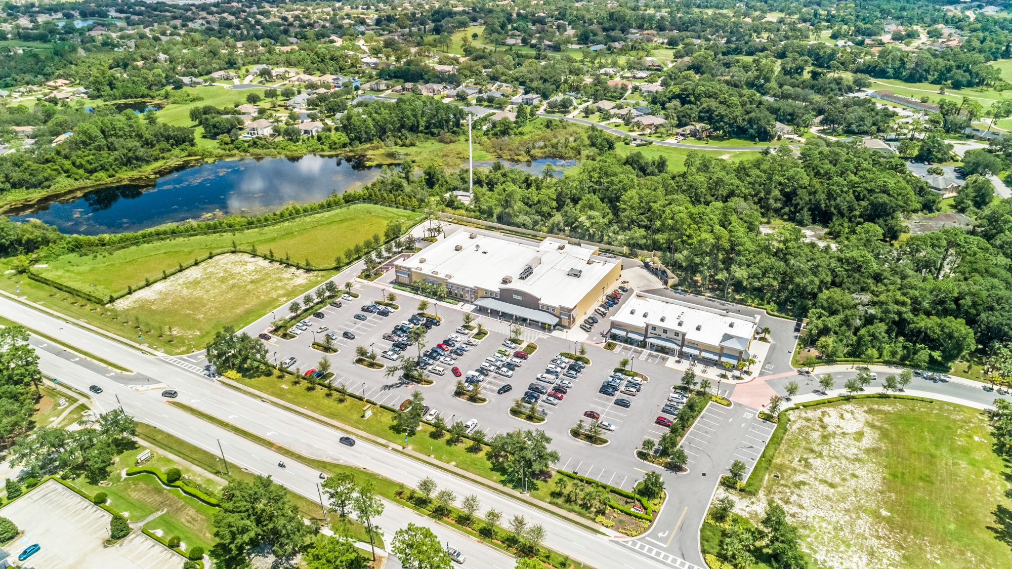 Full aerial overview of a community shopping center showing parking field, road frontage, and surrounding neighborhood