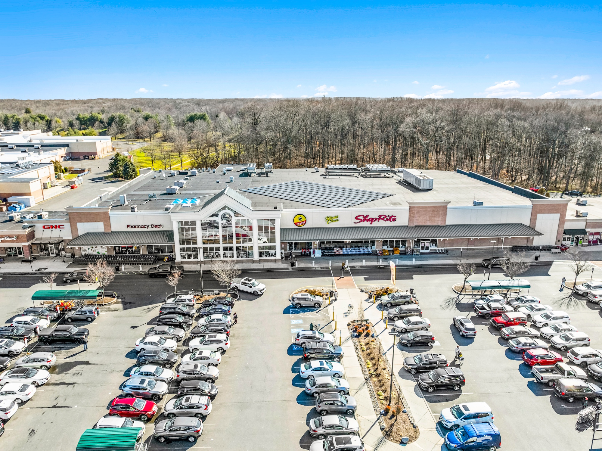 Ground-level aerial of grocery-anchored shopping center showing anchor storefront, signage, and full parking lot