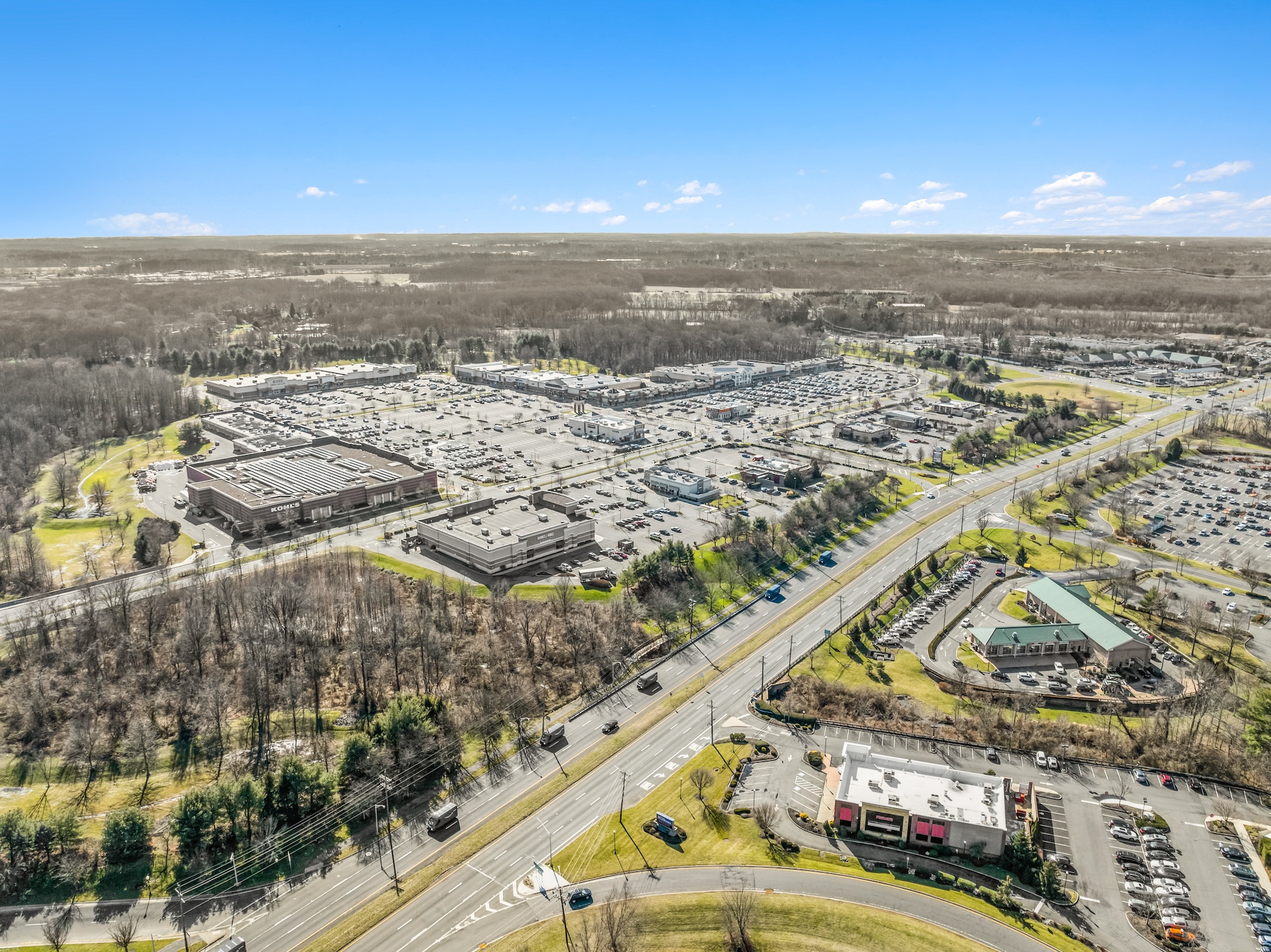 High-altitude aerial photograph of a retail corridor showing multiple shopping centers, highway access, and outparcels