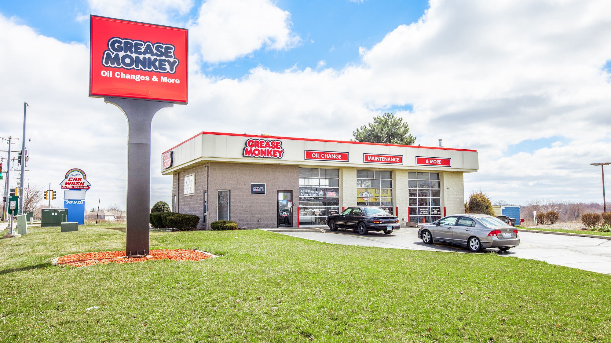 Ground-level photograph of an auto service center with service bay doors, monument signage, and customer parking
