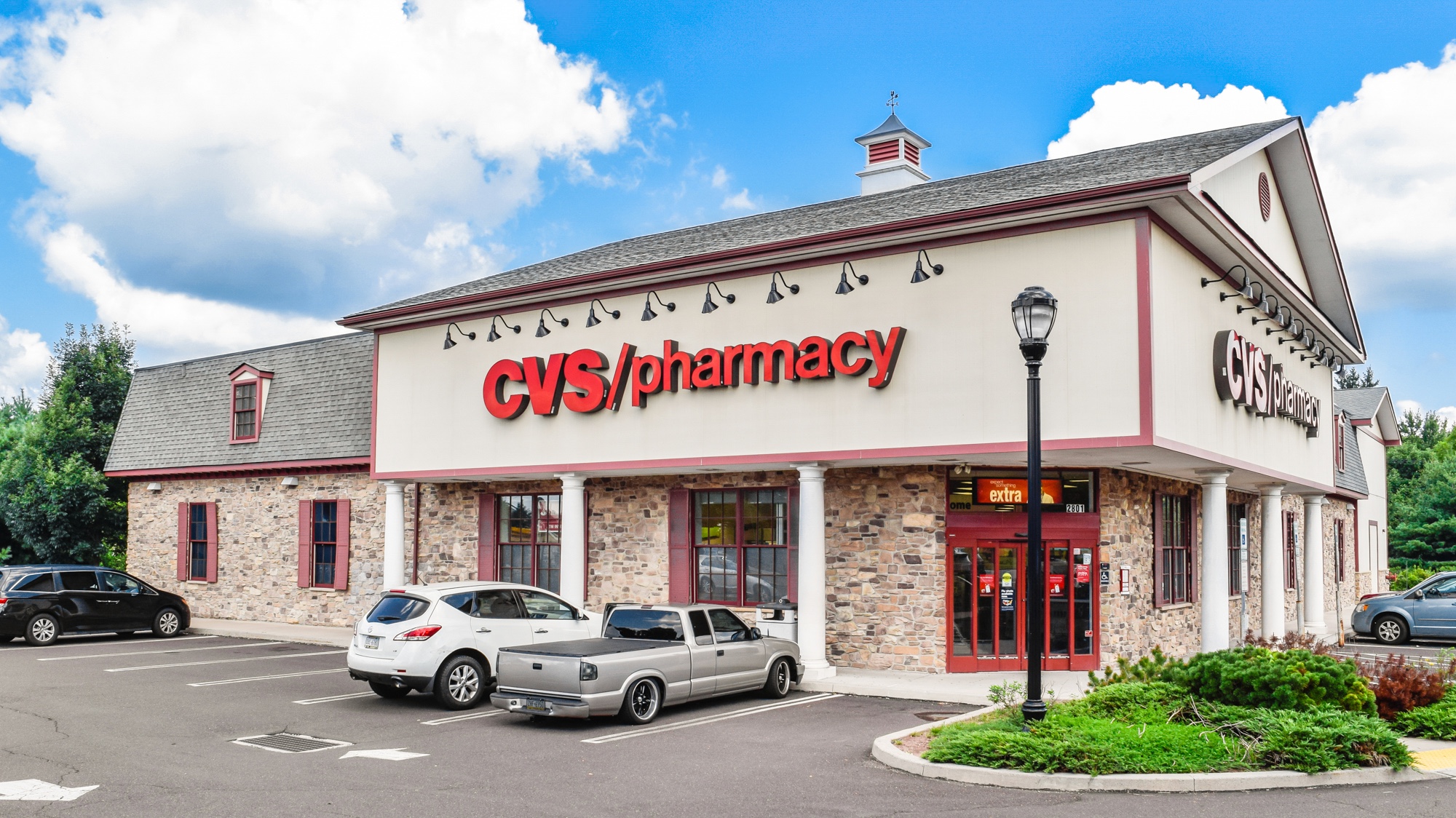 Ground-level photograph of a CVS Pharmacy building facade with stone exterior and customer entrance