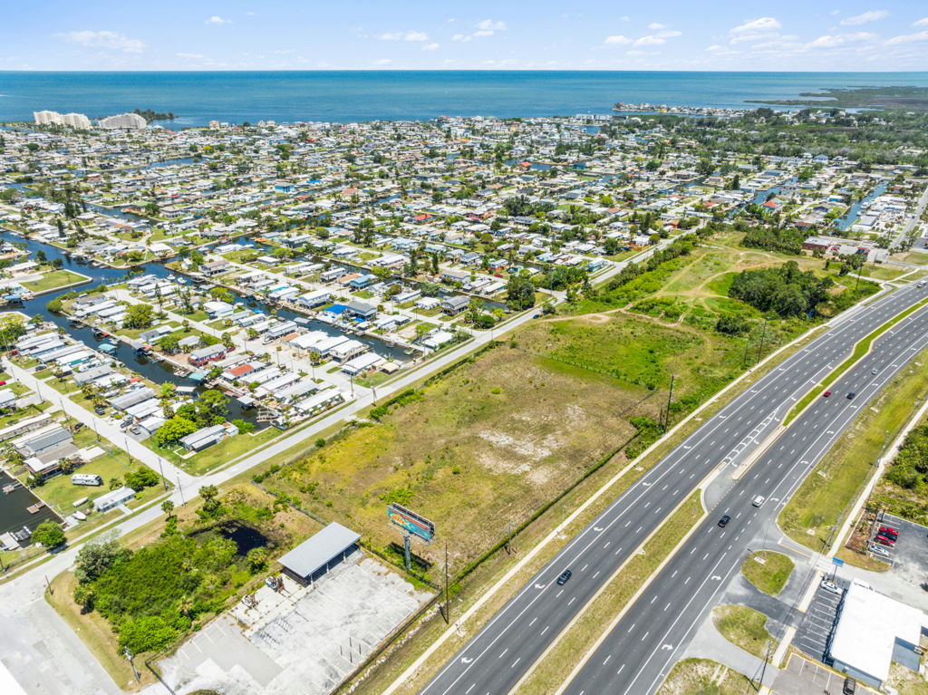 Aerial drone photography of vacant coastal land parcel along highway with ocean and residential views