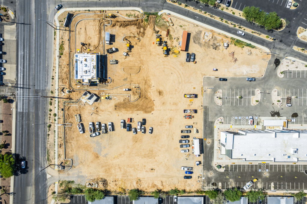 Eagle eye aerial view of active commercial construction site with heavy equipment and adjacent retail