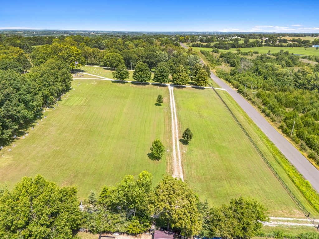 Aerial drone photography of rural green acreage parcel with dirt path and road access