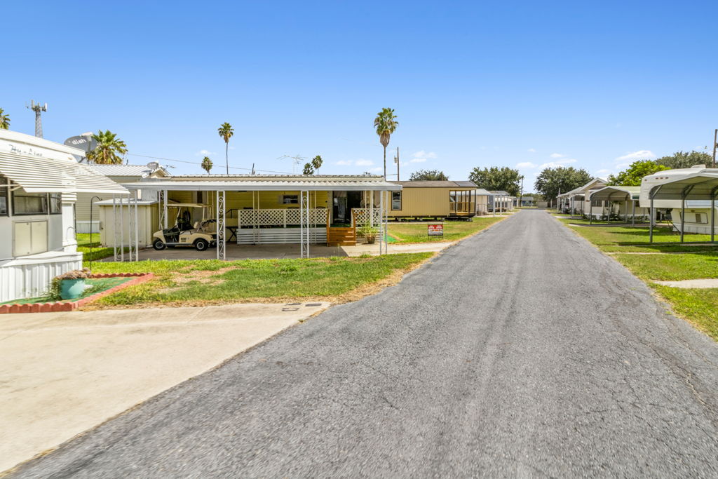 Ground-level photography of mobile home community interior street with covered carports and palm trees