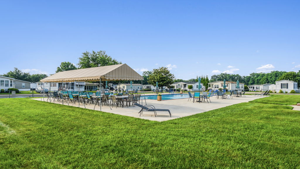 Ground-level photography of mobile home community pool area with covered pavilion and seating