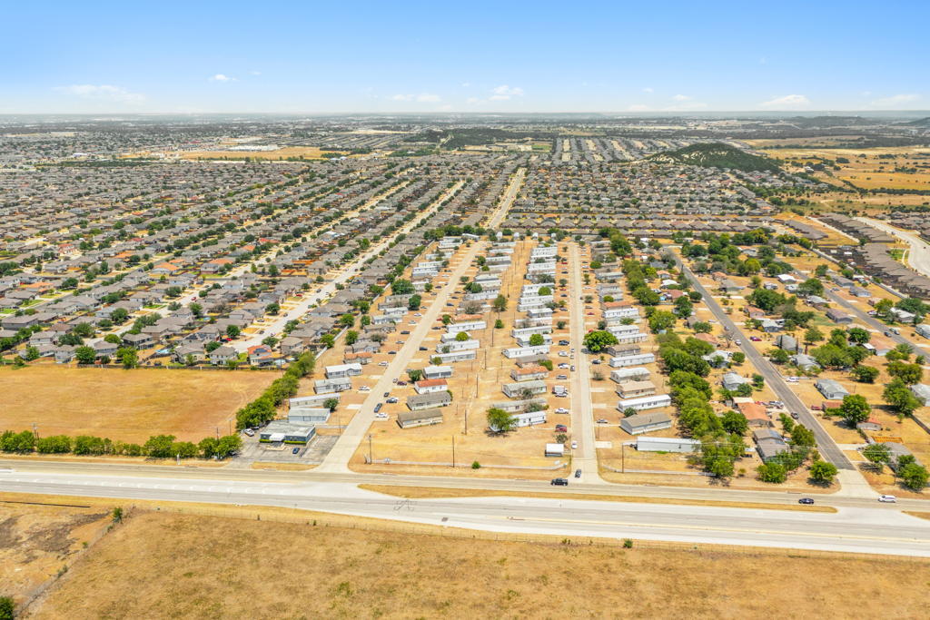 Wide aerial view of large mobile home community along highway with surrounding residential neighborhoods