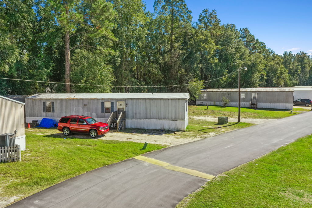 Ground-level photography of rural mobile home community paved road and manufactured homes with trees