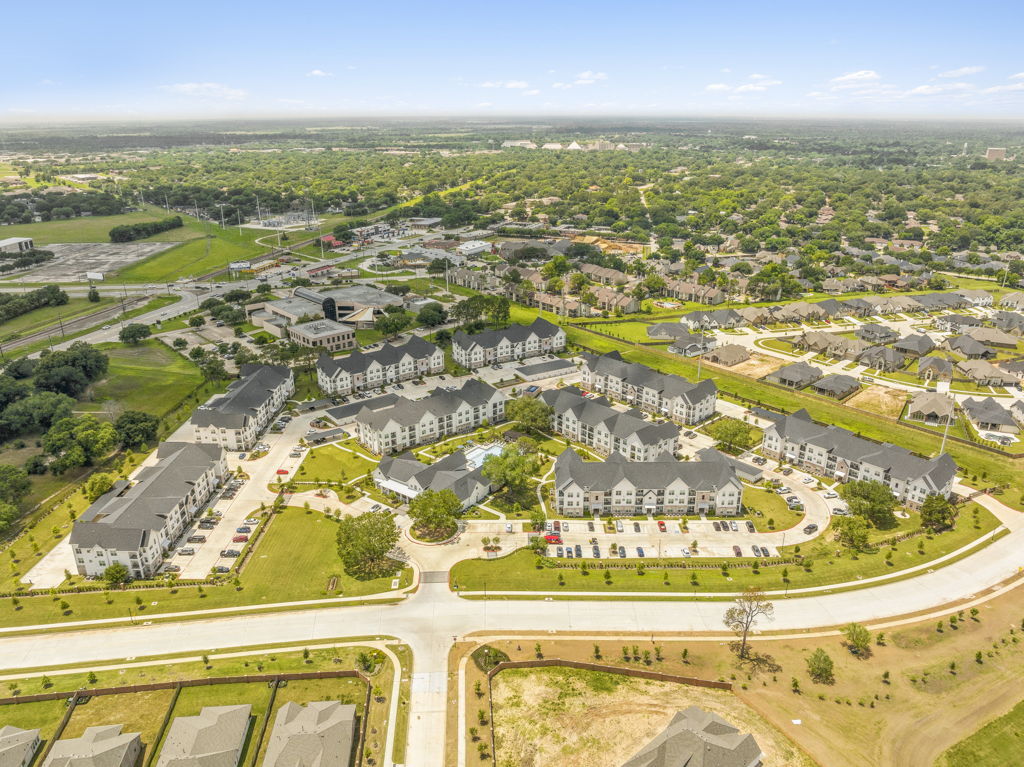 High-altitude aerial drone photography of garden-style apartment community with pool and surrounding development