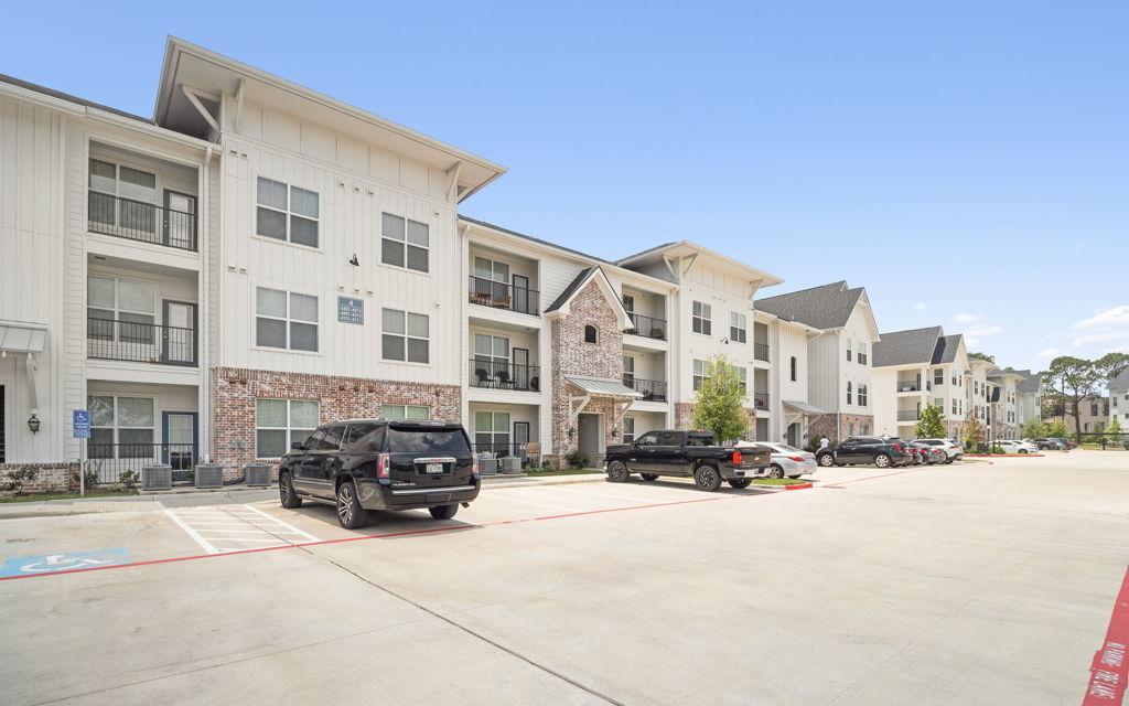 Ground-level photography of three-story suburban apartment building with brick accent and parking