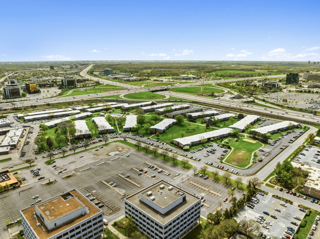 Wide aerial view of suburban apartment complex near highway interchange with parking and green space