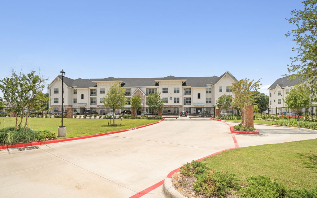 Ground-level photography of suburban apartment community gated entrance with landscaped drive