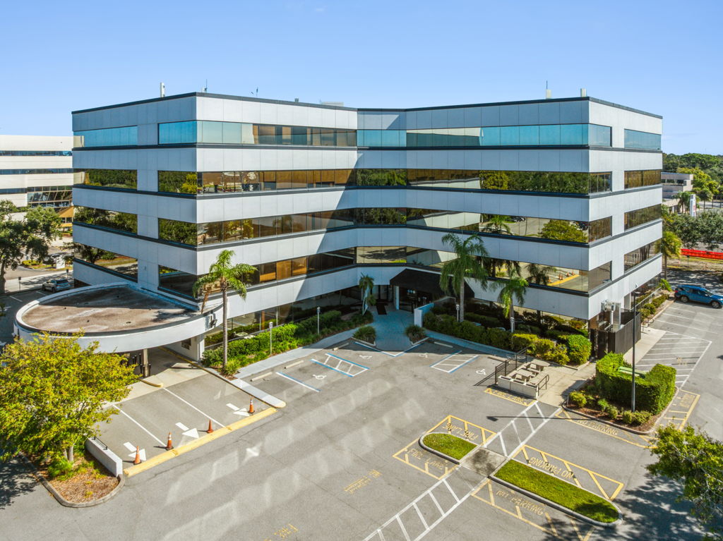 Aerial drone photography of multi-story glass office building with palm trees and visitor parking