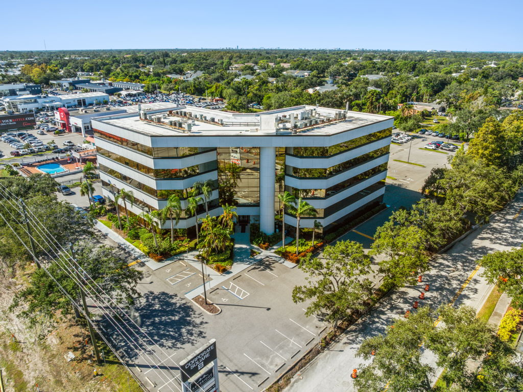 Aerial drone photography of suburban mid-rise office building with surrounding retail and tree canopy