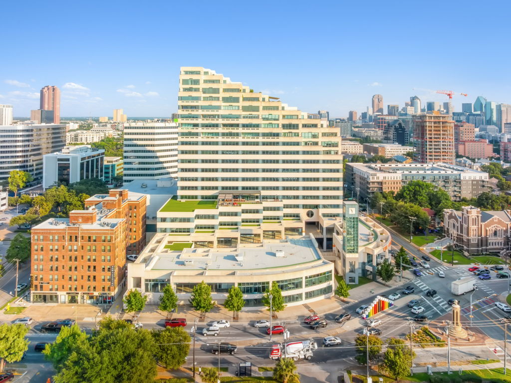 Aerial drone photography of modern urban mixed-use office tower with terraced levels and downtown skyline