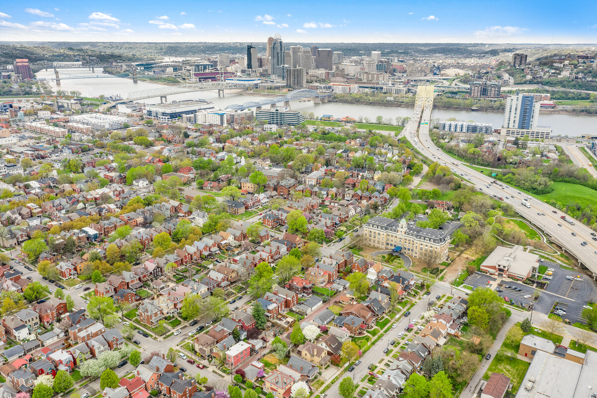 High-altitude aerial photography showing wide area context of a neighborhood, river, and city skyline