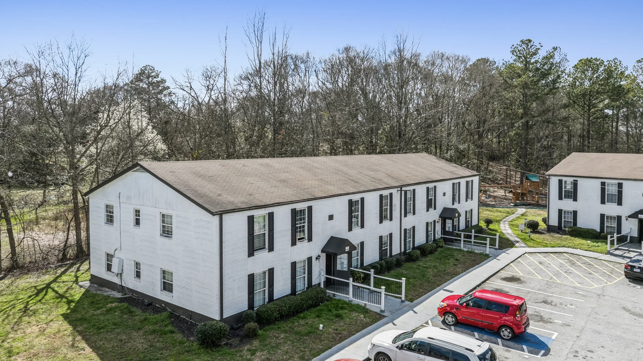Two-story white brick garden-style apartment buildings in wooded suburban setting