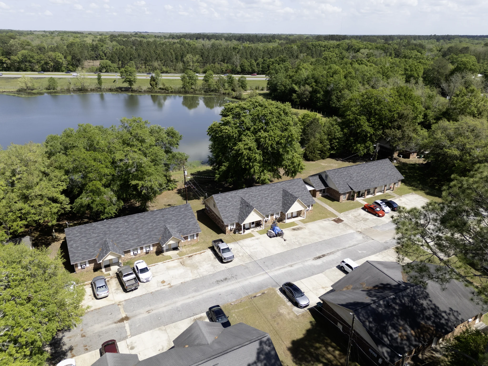 Aerial of single-story workforce rental community with pond and wooded setting
