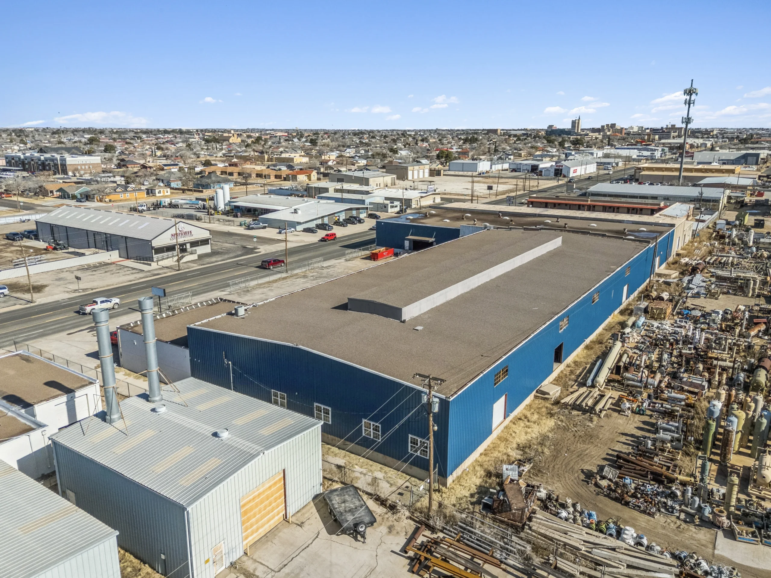 Aerial drone photography of blue metal fabrication warehouse with outdoor equipment yard