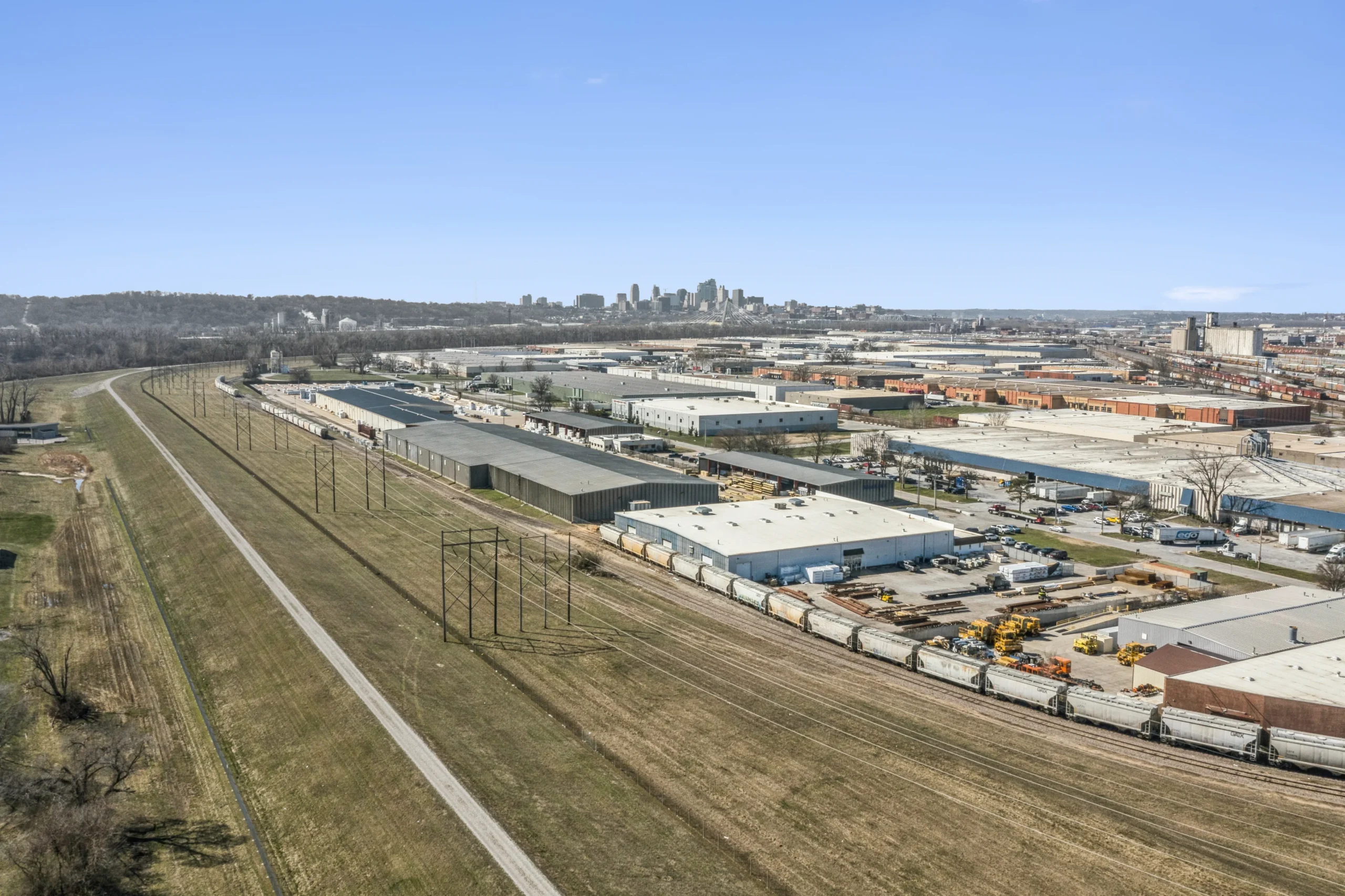 Wide aerial view of industrial park with rail yard and city skyline in background