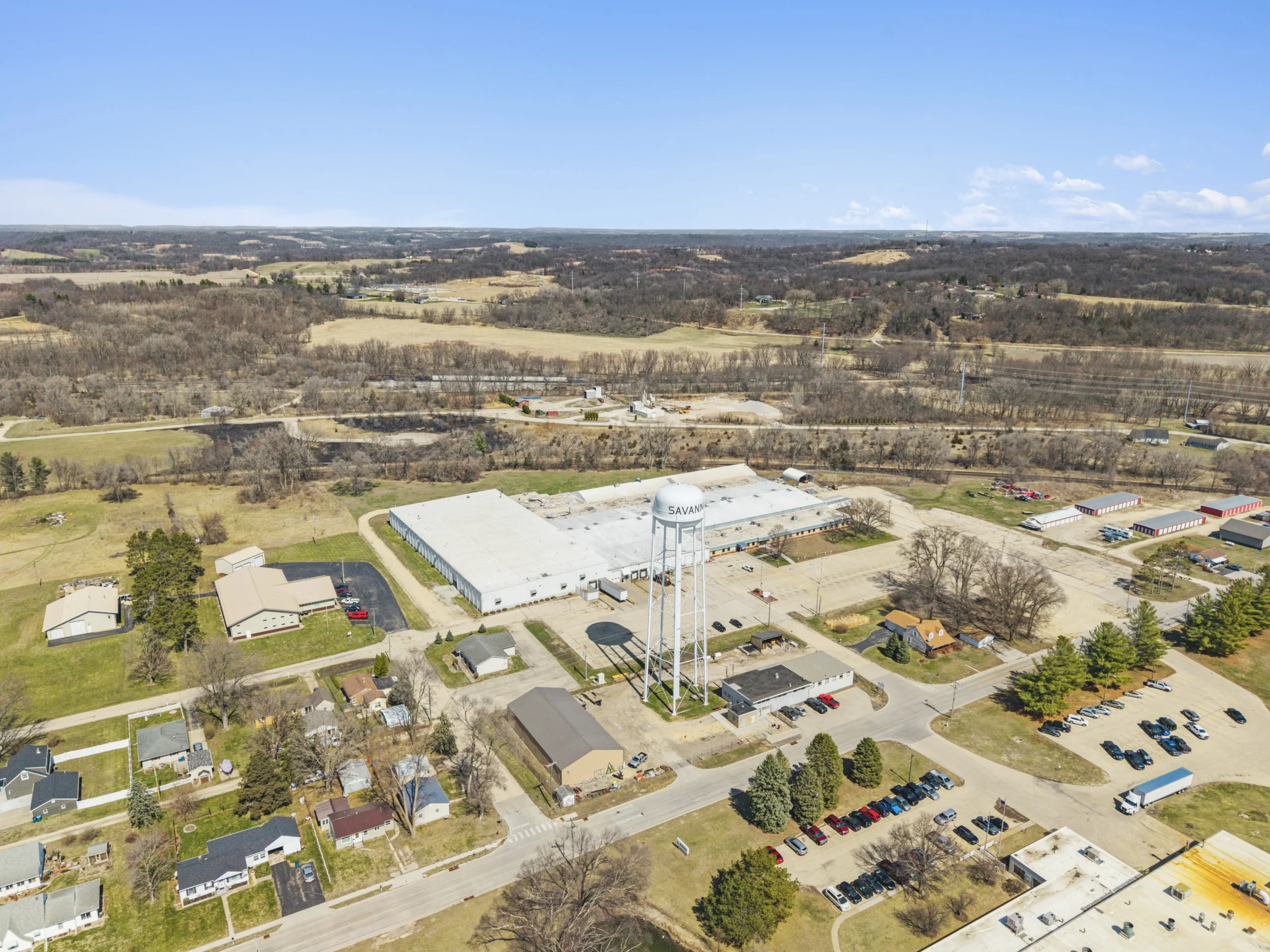 Wide aerial view of rural manufacturing facility with water tower and surrounding community