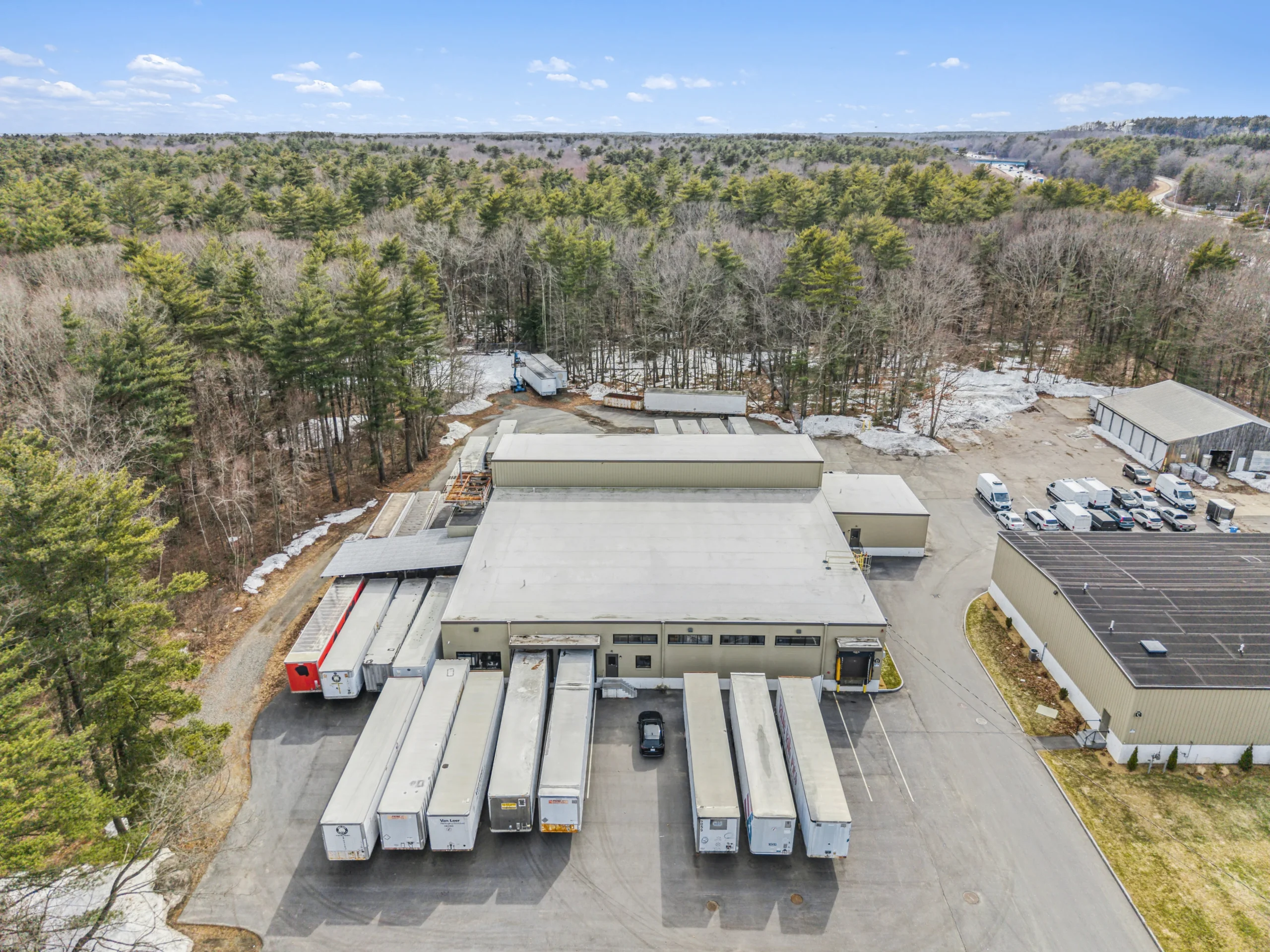 Aerial drone photography of industrial warehouse with trailer docks and forested surroundings