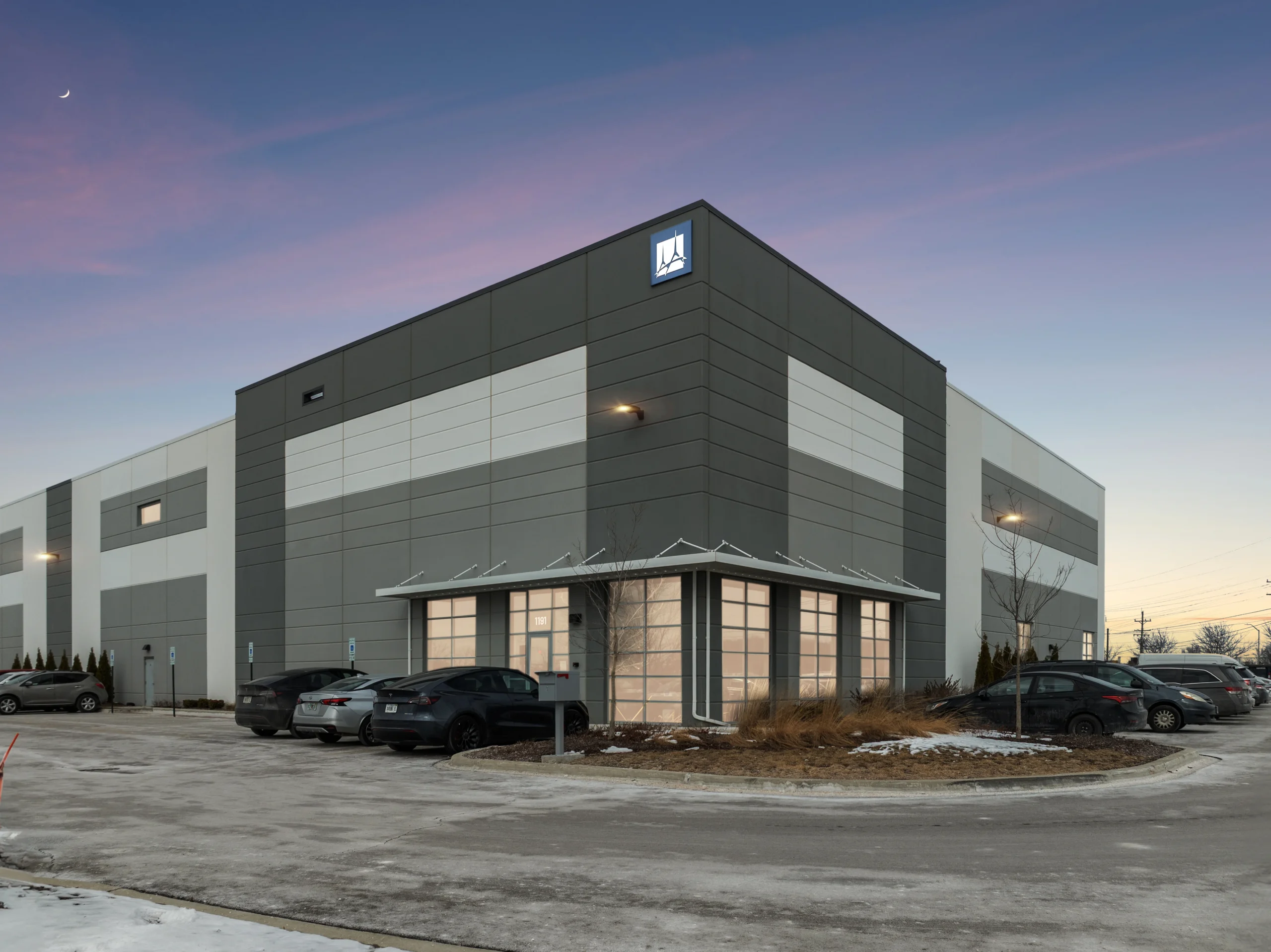 Twilight ground-level photography of modern industrial warehouse entrance with employee parking
