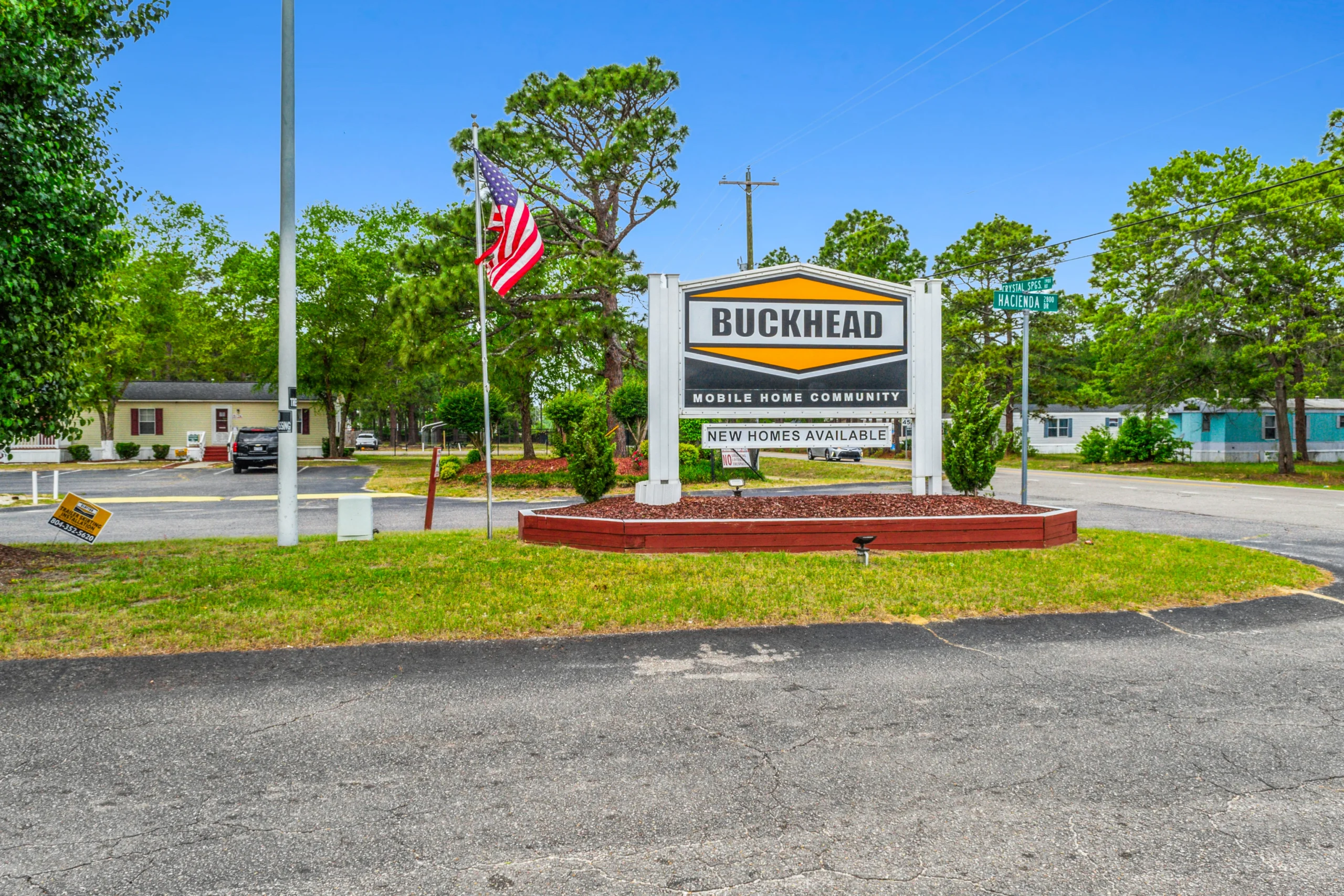 Ground-level photography of mobile home community entrance sign with American flag and landscaping