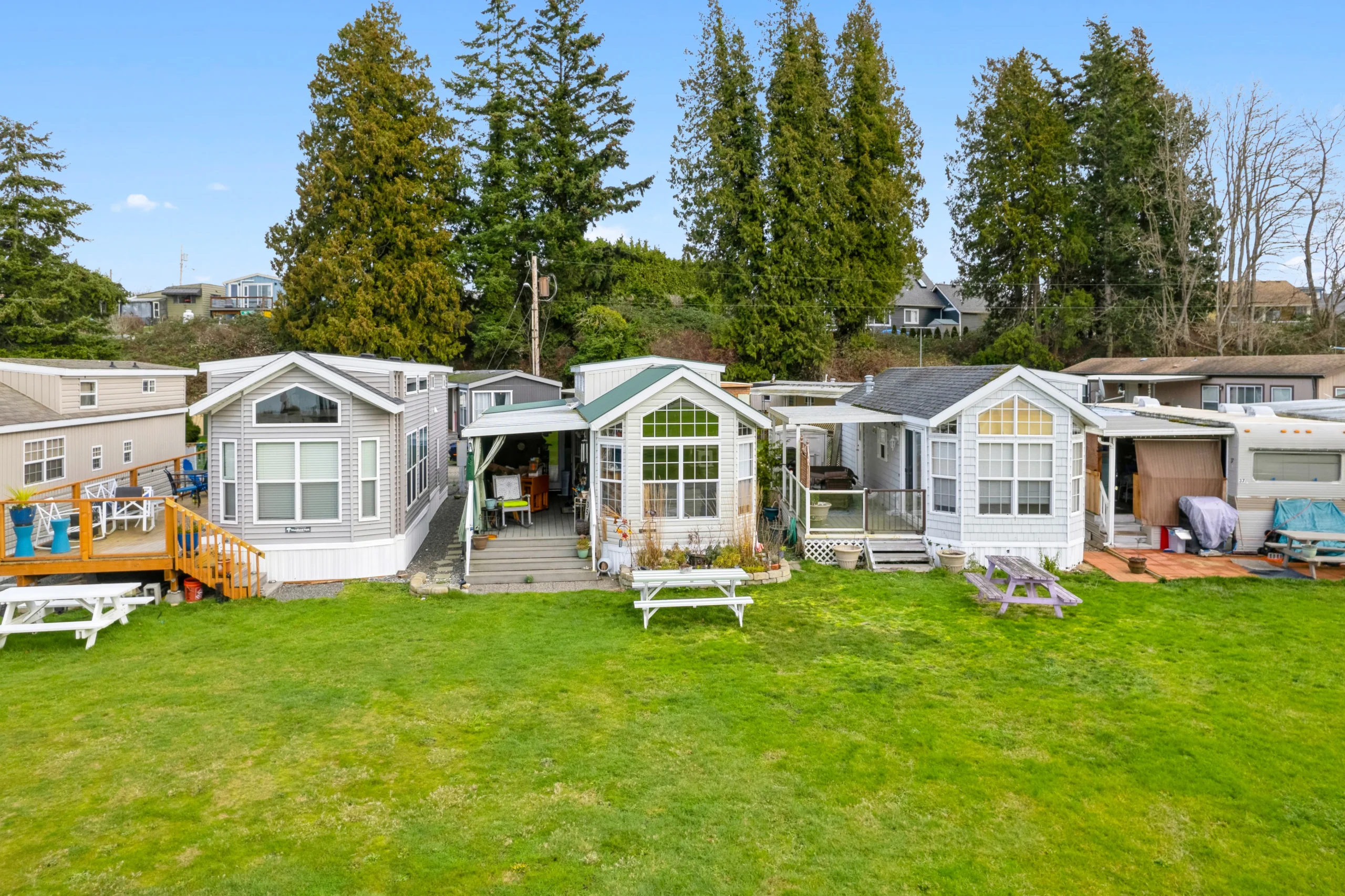 Ground-level photography of cottage-style manufactured homes with green lawn and picnic tables near waterfront