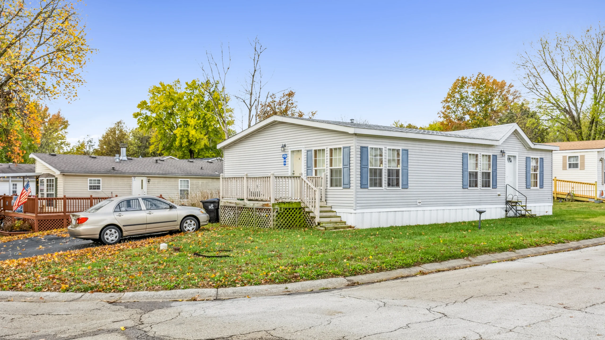 Ground-level photography of manufactured home with blue shutters and front porch in community setting