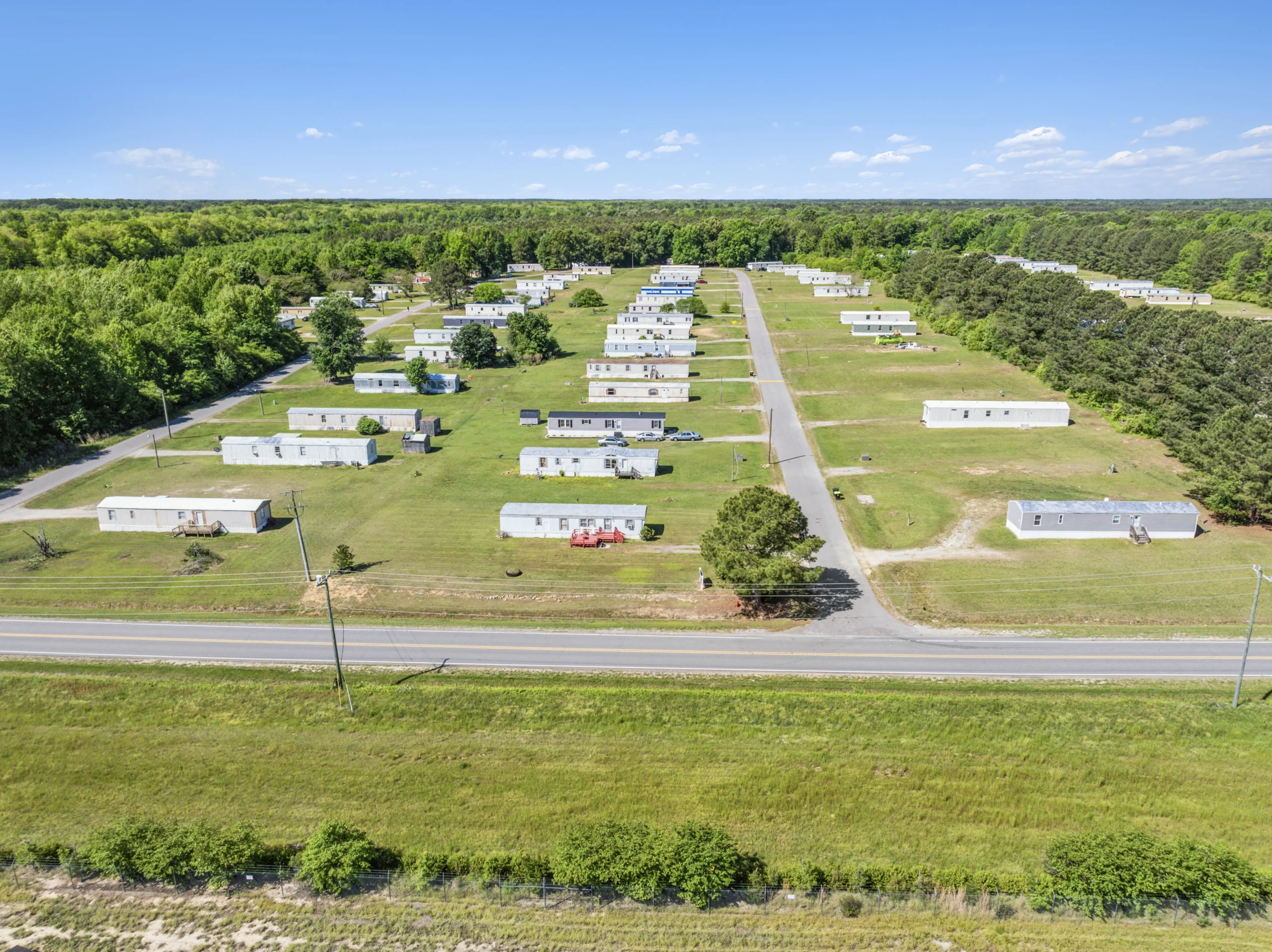Aerial drone photography of rural scattered-site mobile home community along highway with green lots