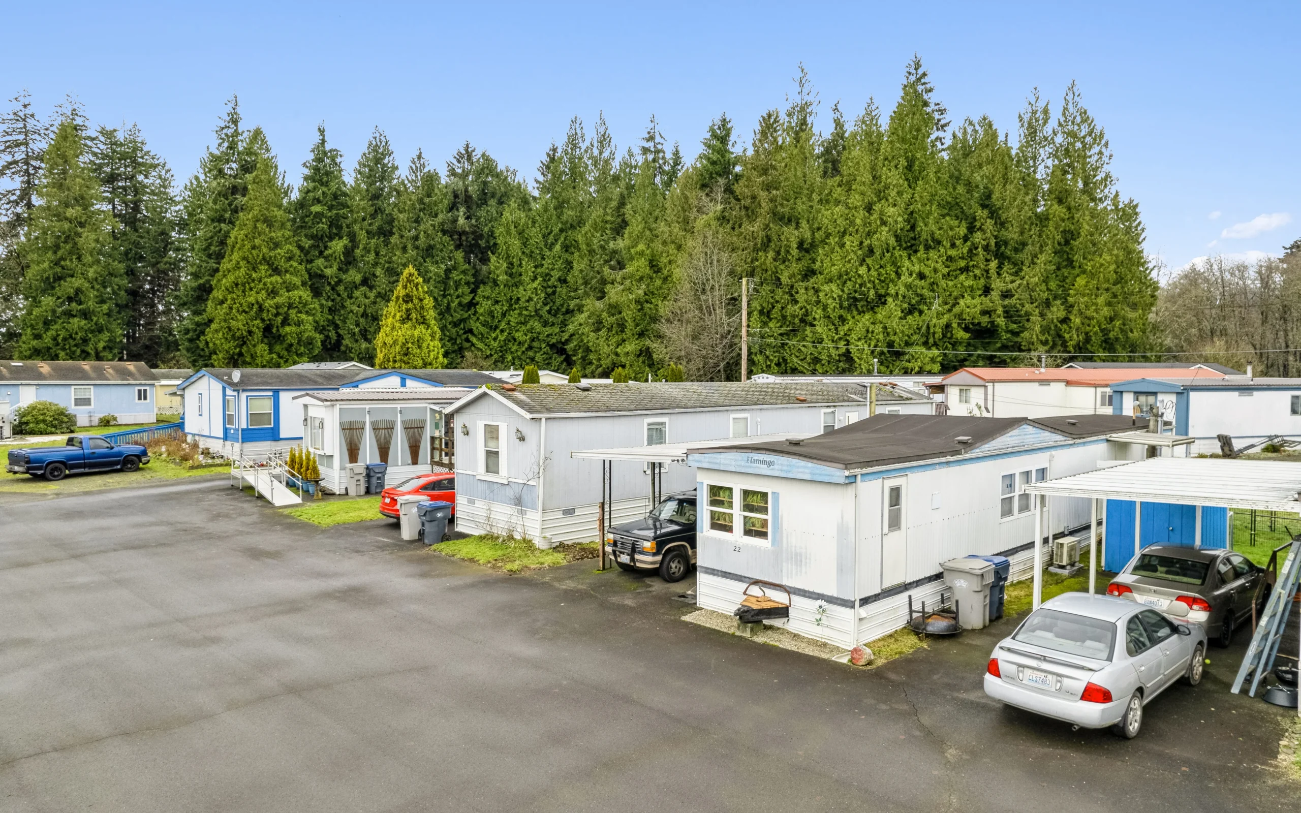 Aerial photography of small mobile home community with paved parking and evergreen tree backdrop