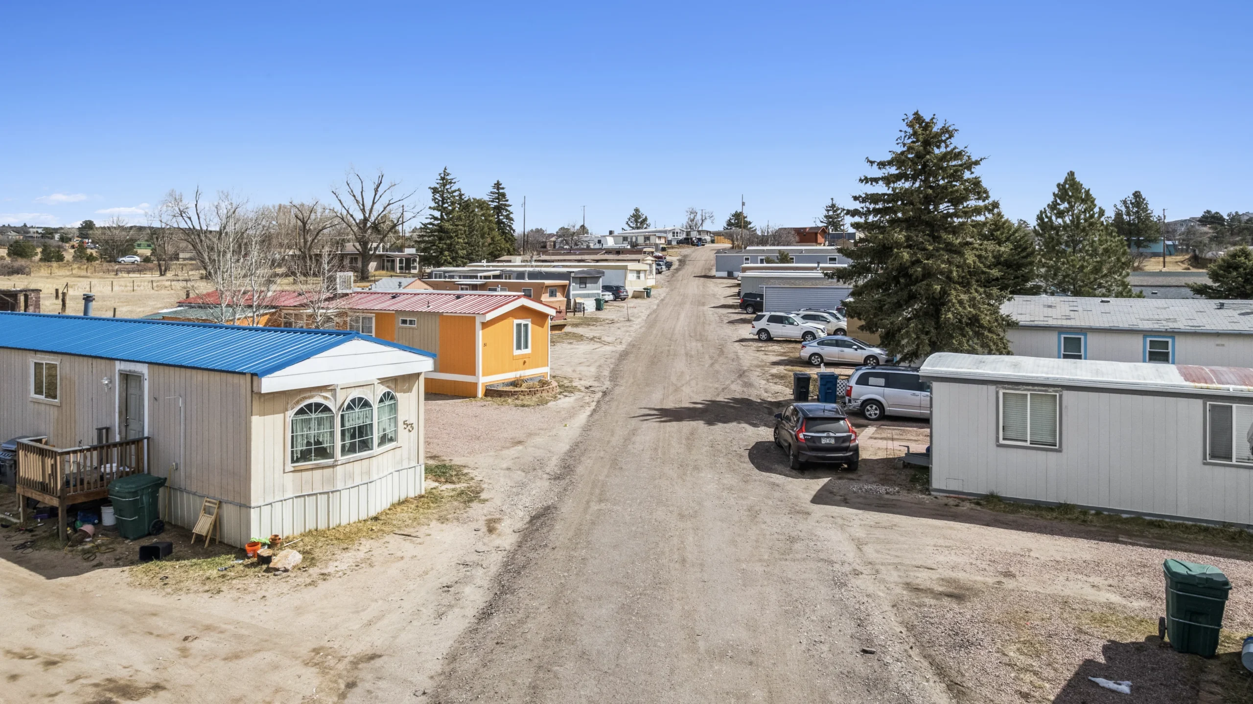 Ground-level photography of western mobile home community with gravel road and colorful units