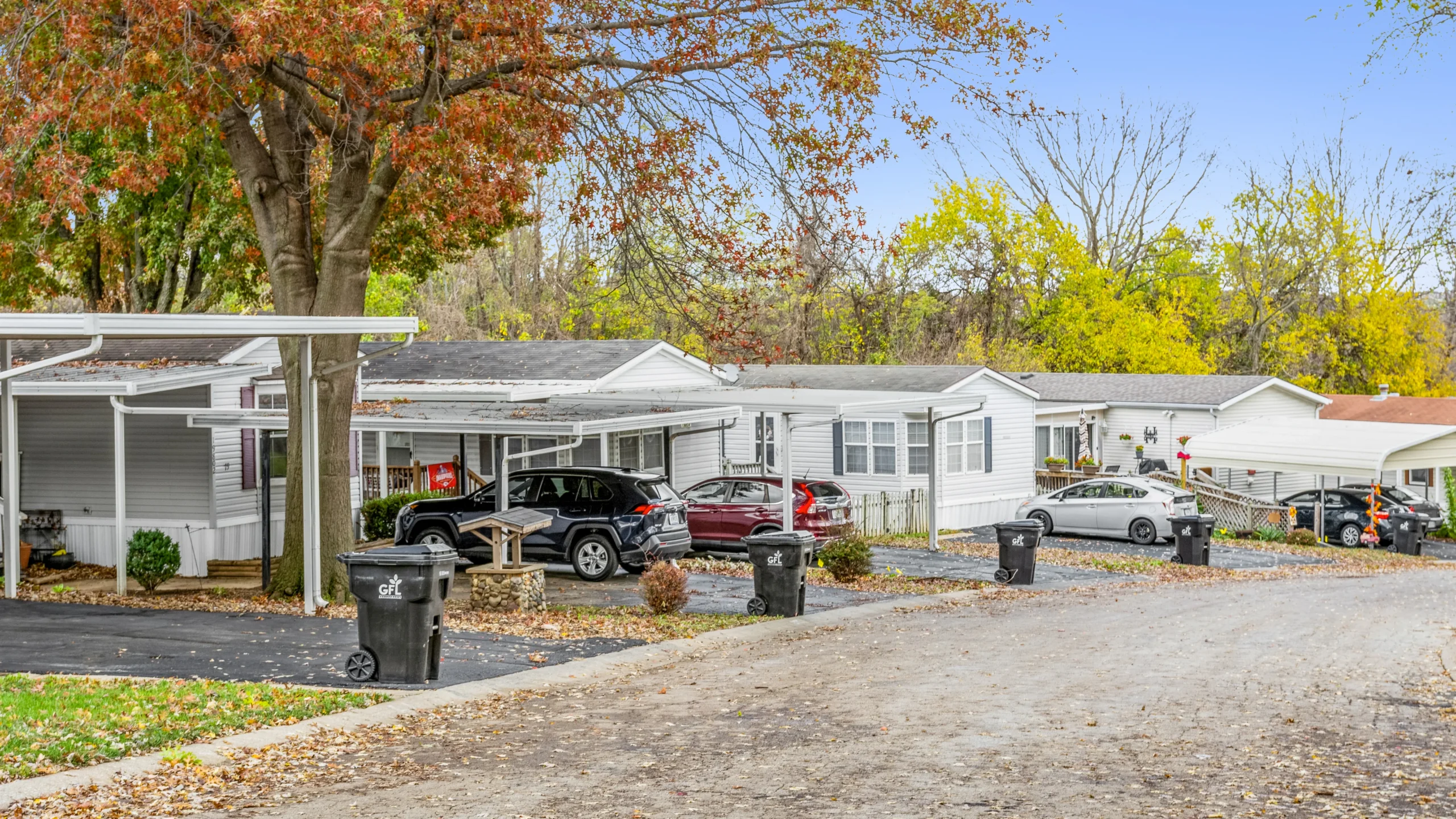 Ground-level photography of wooded mobile home community with carports and autumn trees