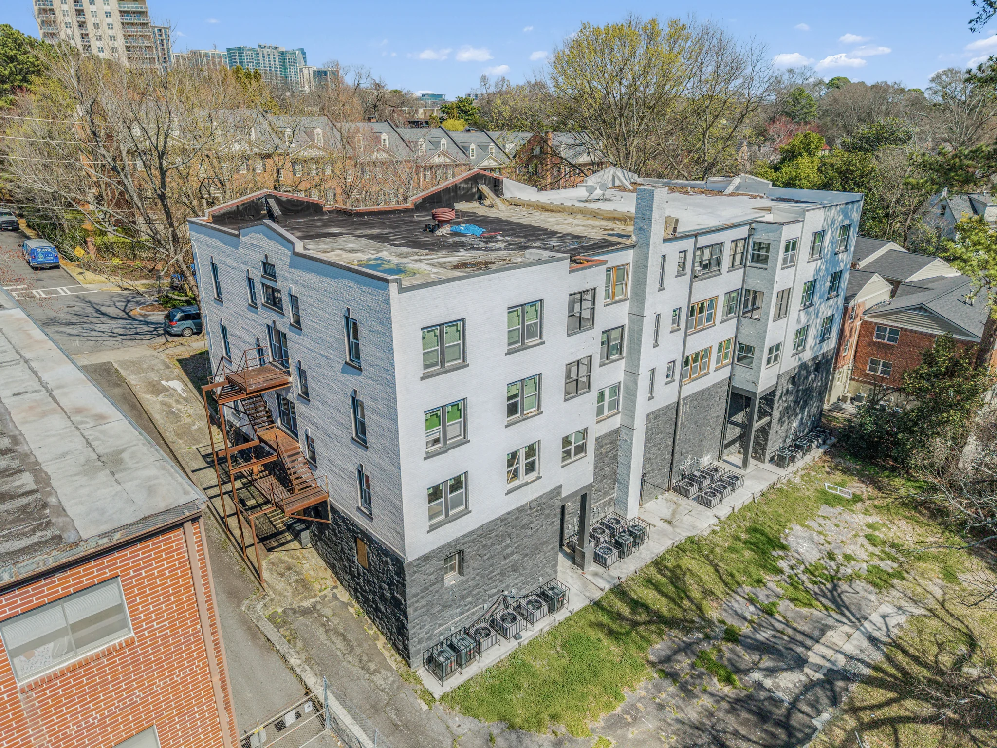 Four-story urban infill apartment building with painted brick exterior and high-rise skyline backdrop
