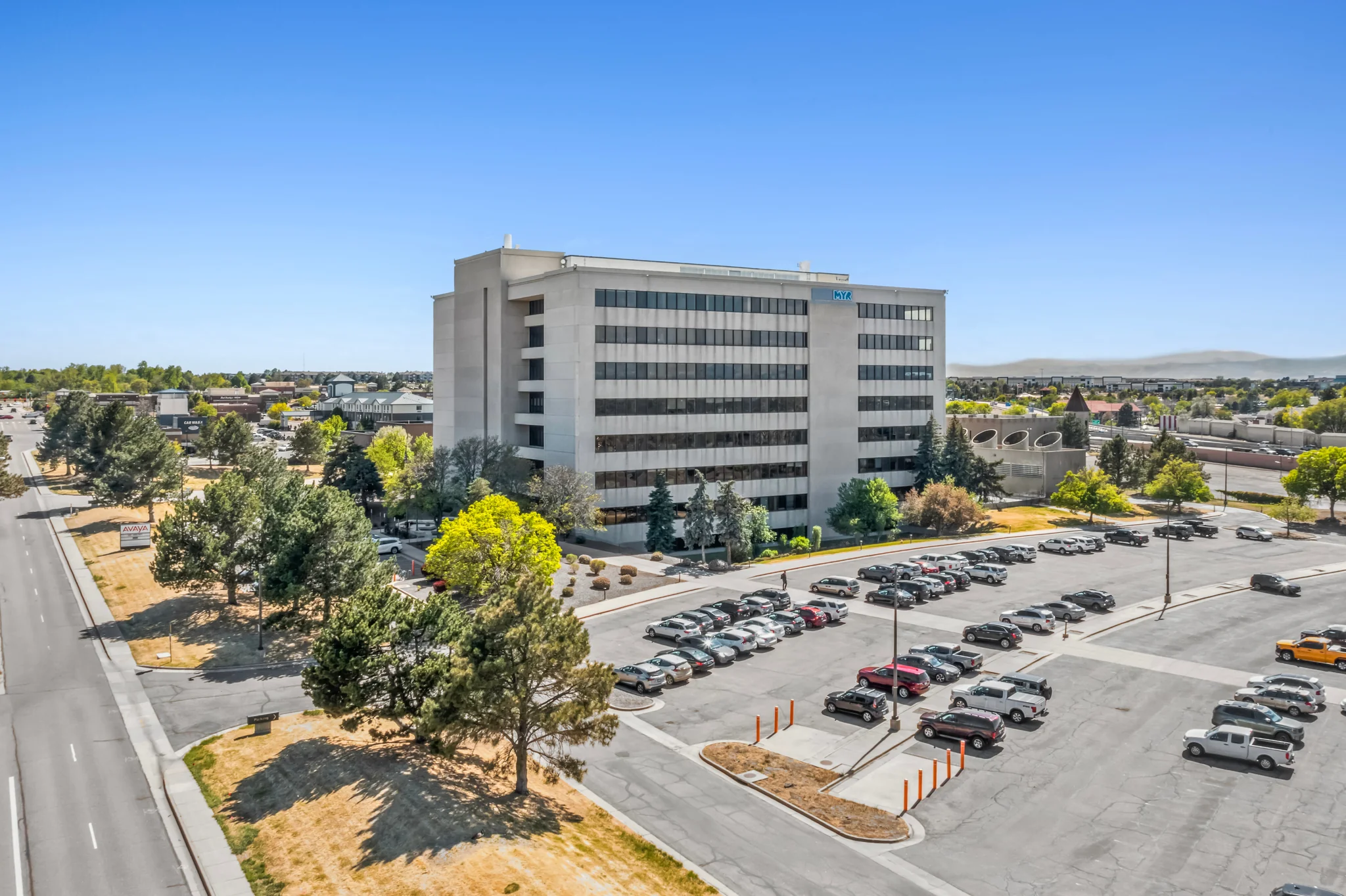 Six-story multi-tenant suburban office building with mountain backdrop and surface parking