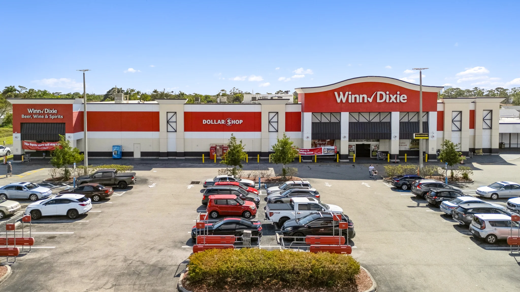 Aerial photograph of a single-tenant Winn-Dixie grocery anchor with attached Beer/Wine/Spirits and Dollar Shop banners, large parking field, and surrounding South Florida trade area