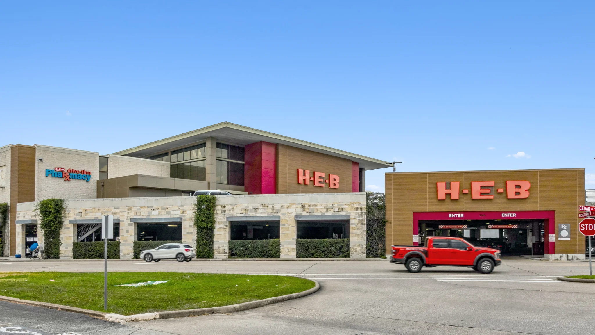 Ground-level photograph of a single-tenant H-E-B grocery store with attached drive-through pharmacy, modern architecture, and street frontage