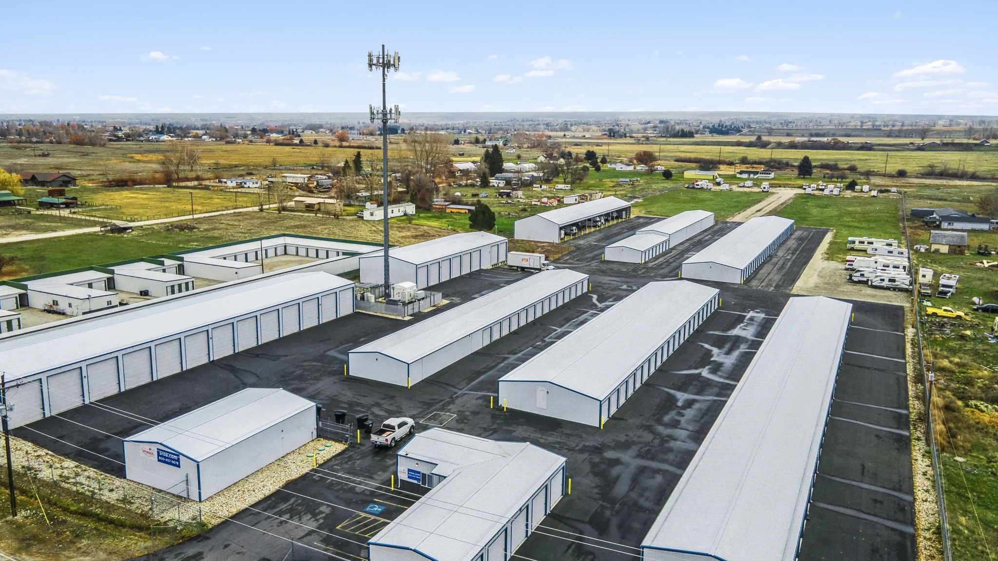 Aerial photograph of a single-tenant self-storage facility with multiple drive-up storage buildings, paved drive aisles, and surrounding agricultural land