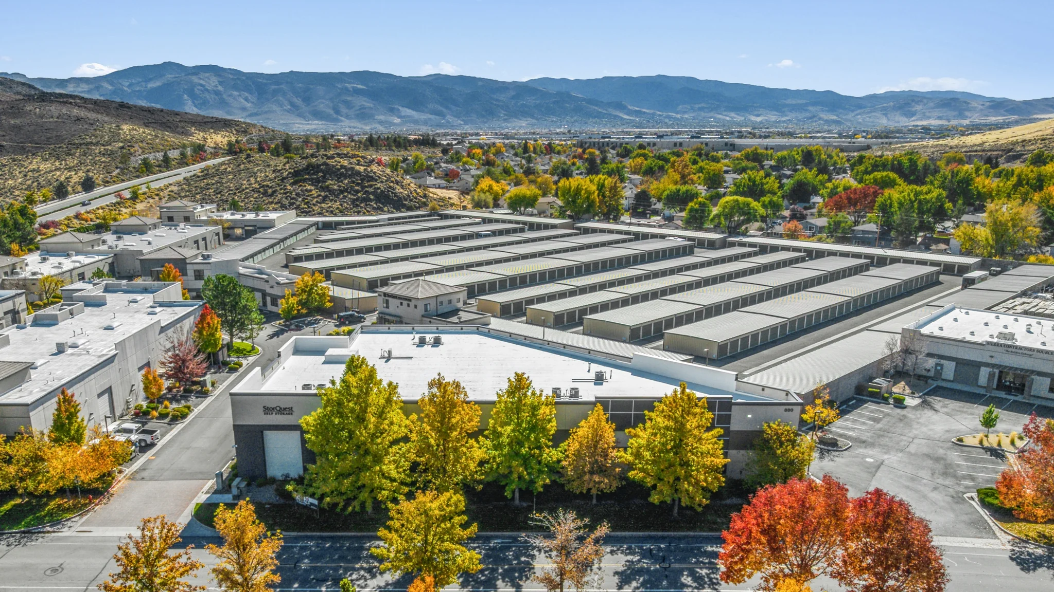 Aerial photograph of a single-tenant StorQuest Self Storage facility with multi-row drive-up storage buildings, front office, and mountain backdrop