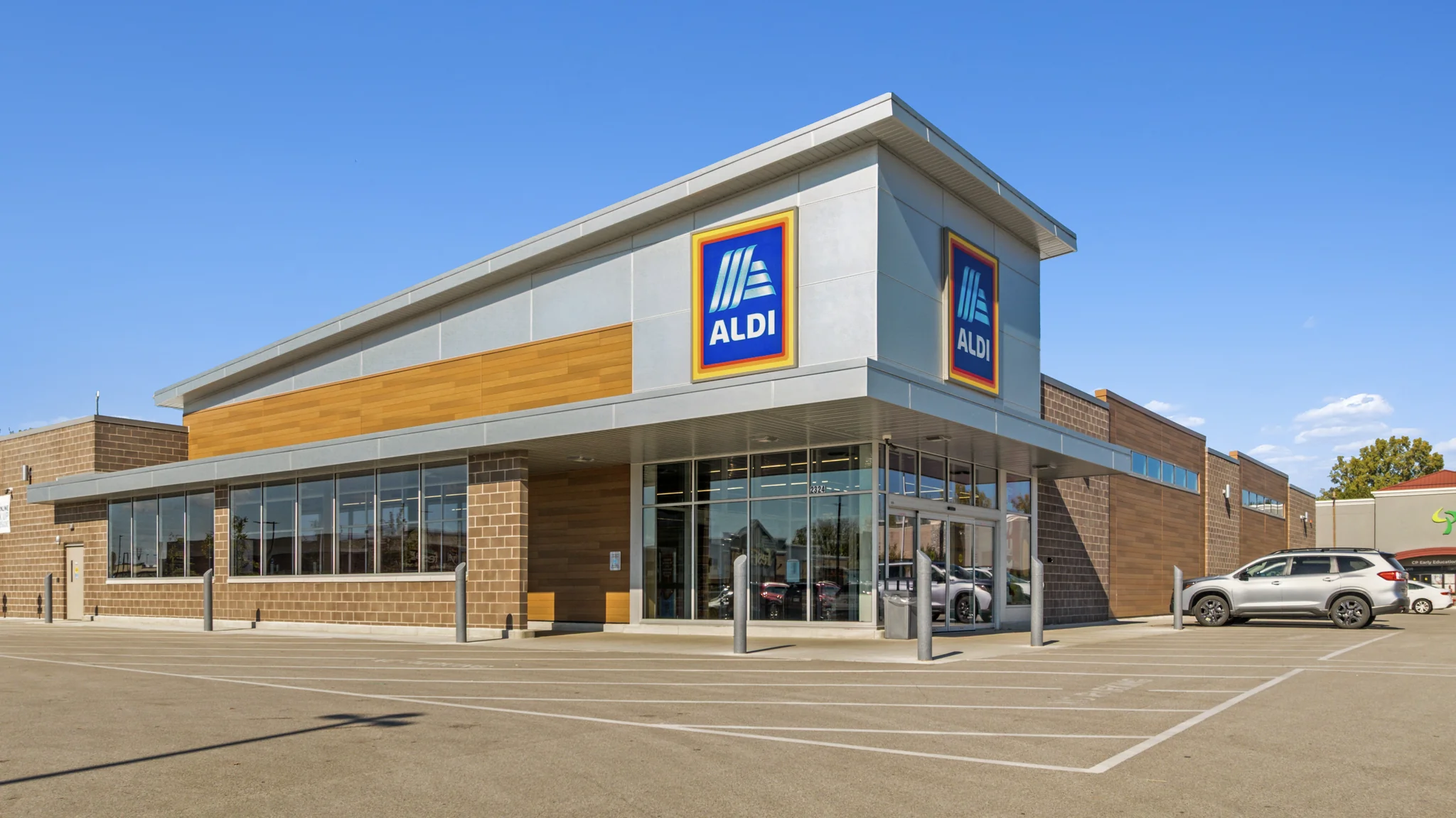 Ground-level photograph of a single-tenant Woods Supermarket with deli, bakery, meat, and produce department signage and large parking field