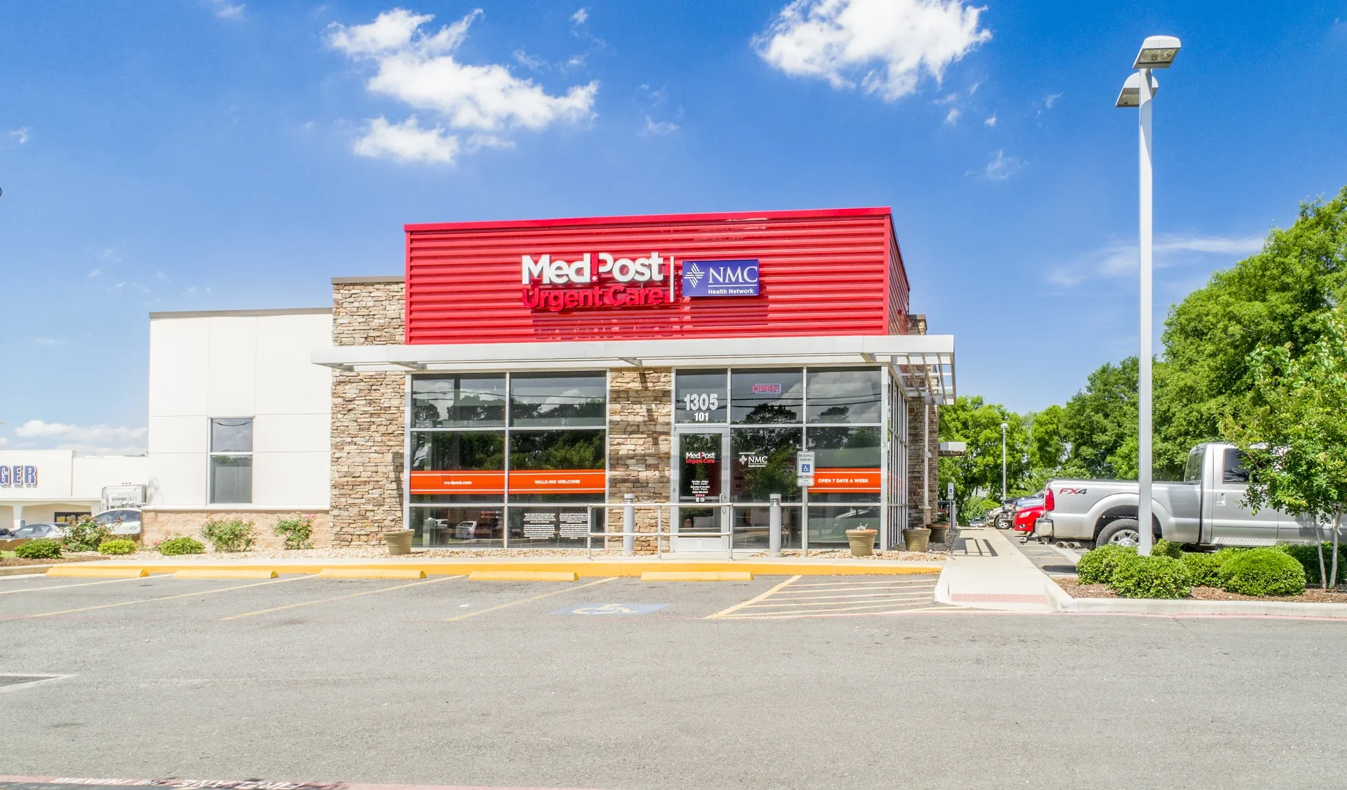Ground-level photograph of a single-tenant MedPost Urgent Care building with stacked-stone facade, red corrugated metal awning, and patient parking adjacent to Kroger
