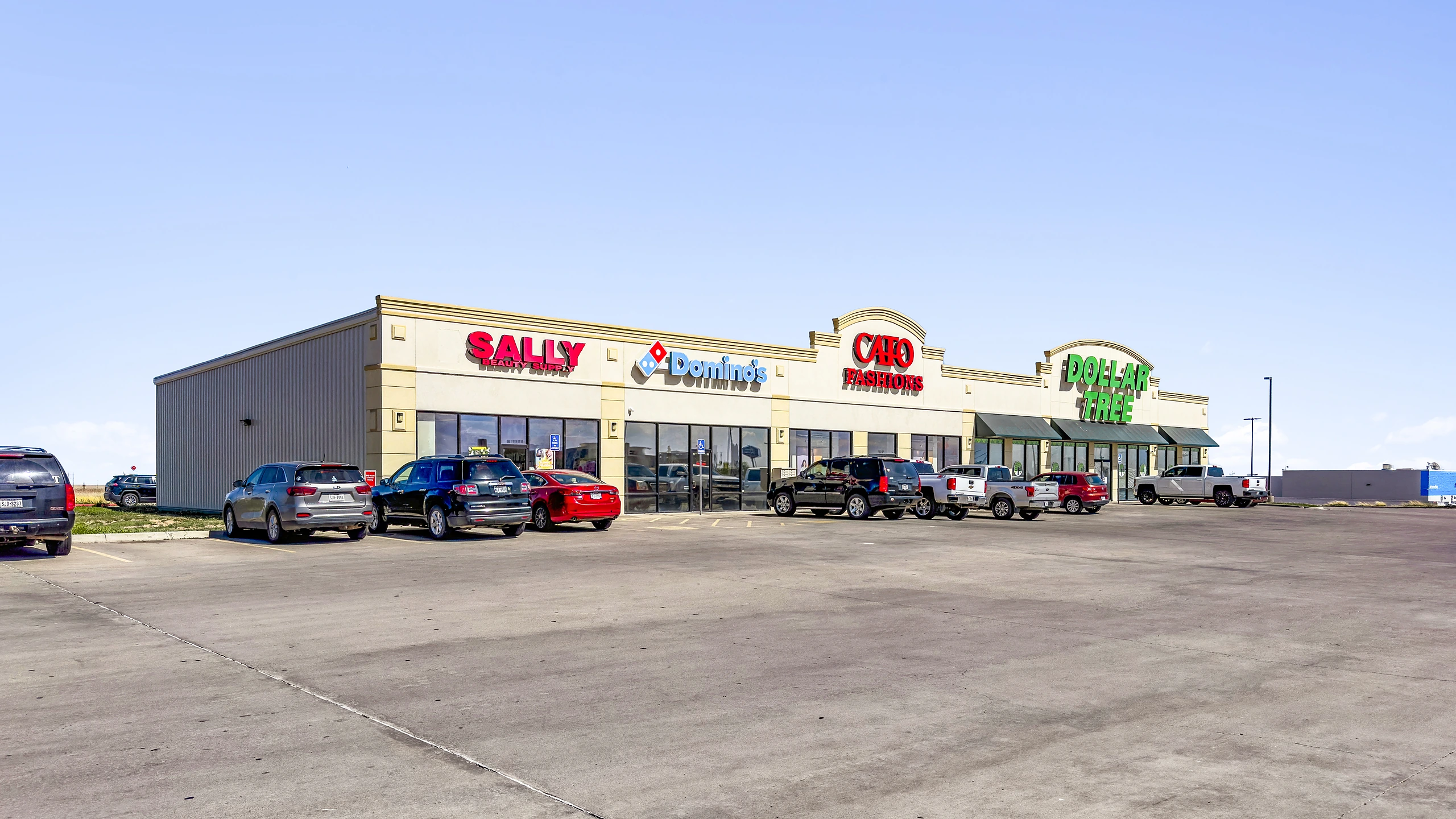 Ground-level photograph of a discount-anchored multi-tenant retail center with dollar store, fashion, beauty supply, and quick-service restaurant inline tenants
