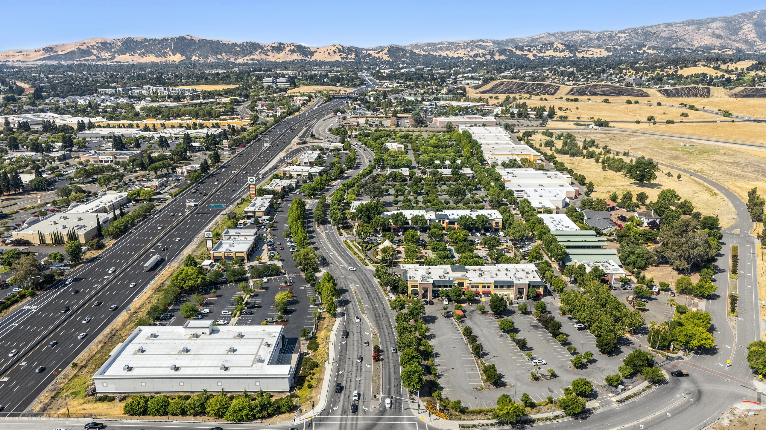 High-altitude aerial of a retail corridor along a major highway with multiple multi-tenant centers