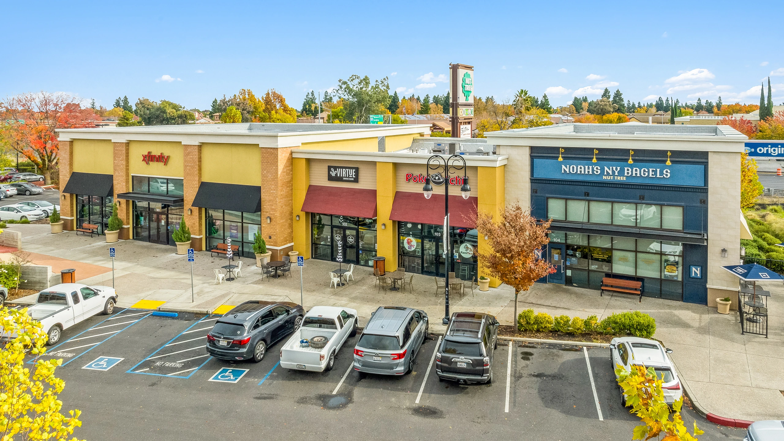 Ground-level photograph of inline strip center storefronts with local service tenants and autumn landscaping