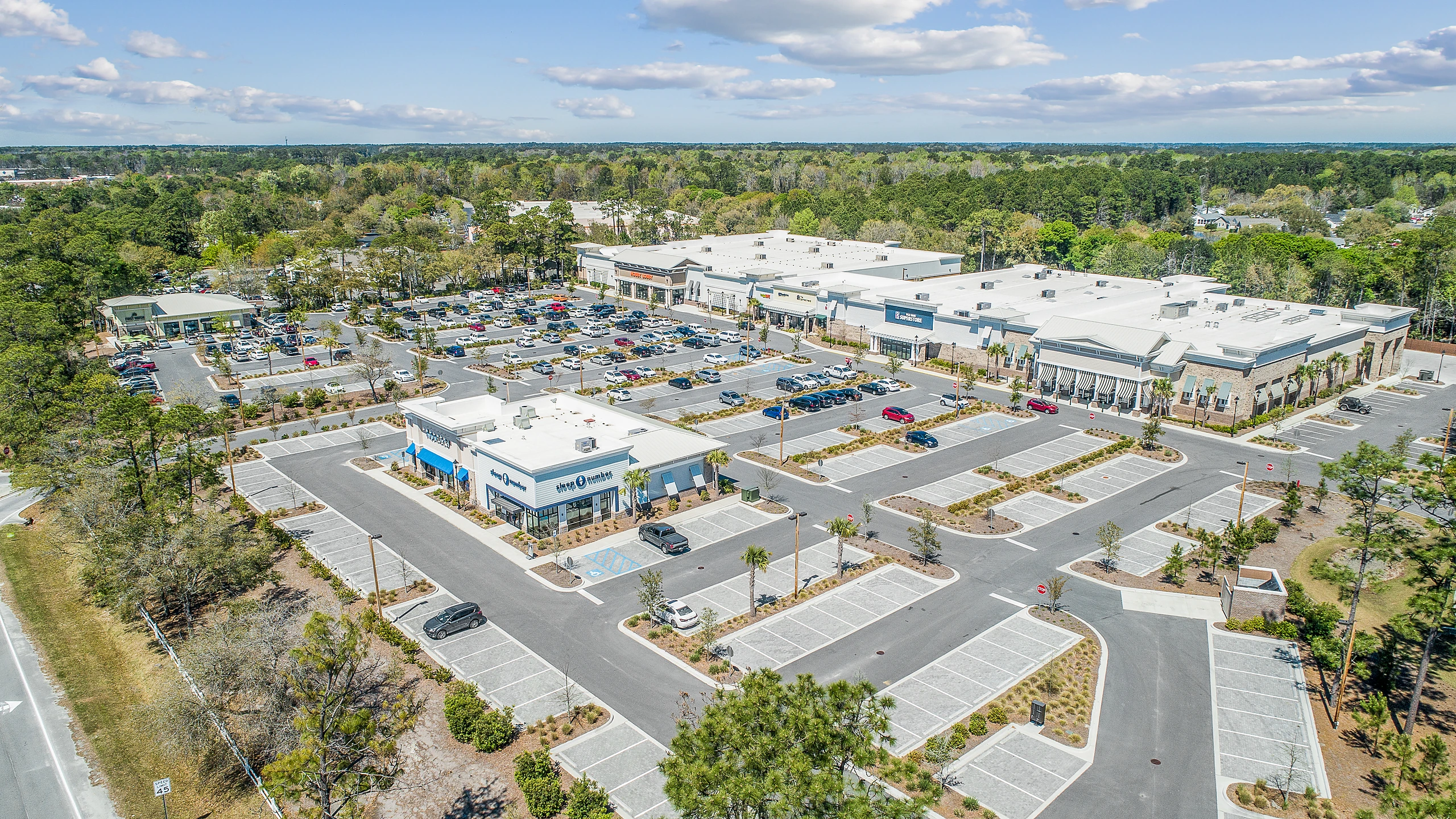 Aerial photograph of a newly built retail center with freestanding pad buildings, fresh inline storefronts, and new parking field
