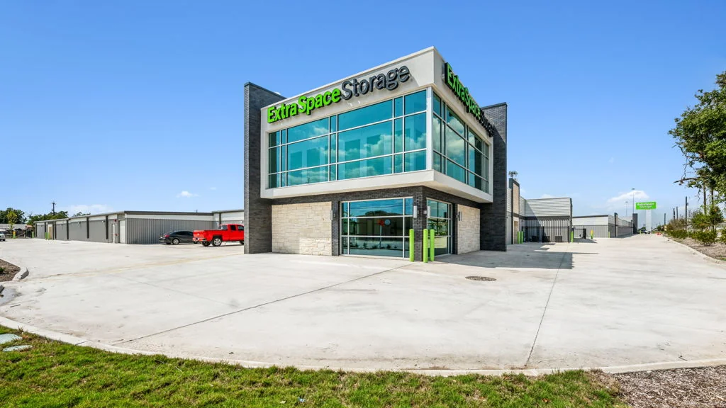 Ground-level photograph of a single-tenant Extra Space Storage facility with two-story glass office building, branded signage, and drive-up storage buildings