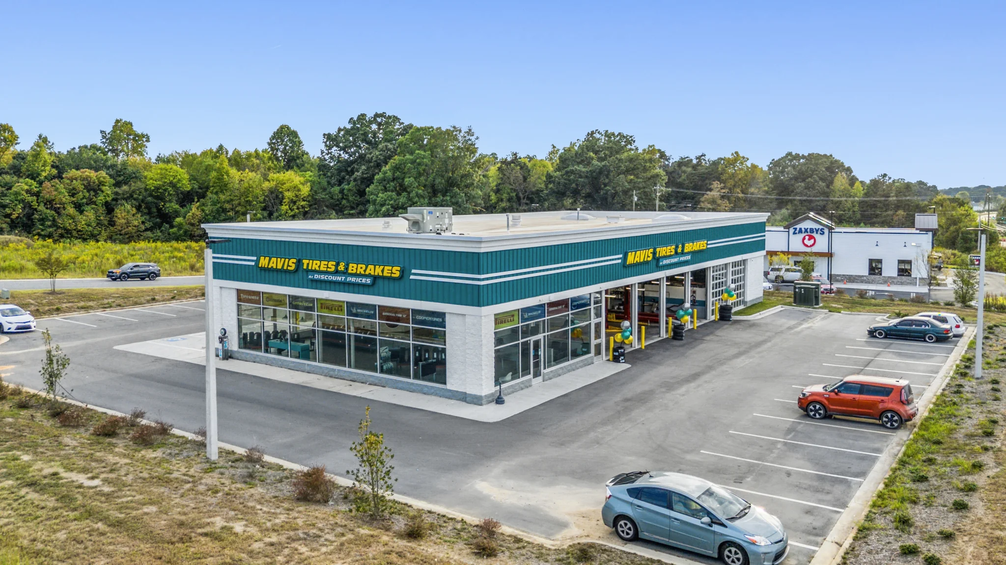Aerial photograph of a single-tenant Mavis Tires and Brakes auto service building with open service bays, branded signage, and customer parking