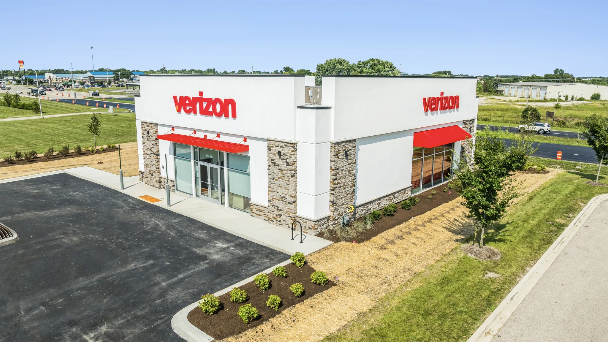 Aerial photograph of a newly built single-tenant Verizon wireless store with stone facade, red awnings, and highway frontage